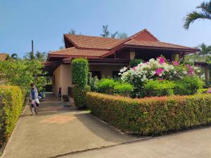 a man walking past a house with bushes and flowers at Seabreeze 145 by malai in Rayong