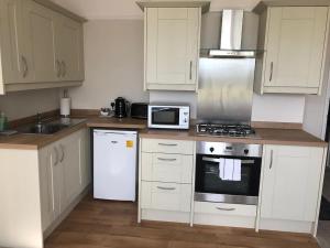 a kitchen with white cabinets and a stove and a microwave at SeaBright; one bed apartment with garden and parking in Mundesley