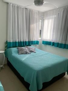 a bedroom with a bed with blue sheets and white curtains at Apartamento cobertura Ubatuba in Ubatuba
