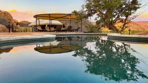 une piscine avec une table, des chaises et un arbre dans l'établissement Twyfelfontein Adventure Camp, à Khorixas