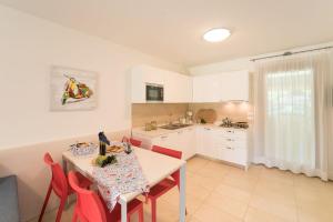 una cocina con mesa con sillas rojas y una cocina con armarios blancos en Villaggio Tamerici, en Lignano Sabbiadoro