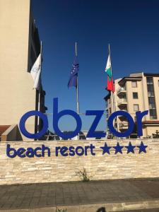 een bord voor een strandresort met vlaggen aan de muur bij Obzor Beach Resort Beachfront in Obzor