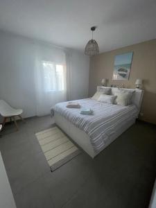 een witte slaapkamer met een groot bed en een stoel bij Cottage Dune in Saint-Jean-de-Monts