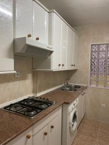 eine Küche mit weißen Schränken, einem Herd und einer Spüle in der Unterkunft Precioso Apartamento en Puertollano in Puertollano