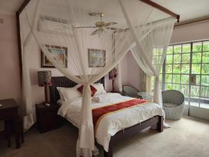 1 dormitorio con cama con dosel y cortinas blancas en Jacaranda Lodge, en Victoria Falls