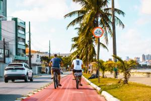 dos hombres montando bicicletas por una calle con palmeras en Ap Manaíra, prático e acolhedor, en João Pessoa