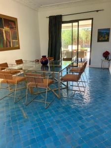a dining room with a glass table and chairs on a blue tile floor at Villa Madina in Dar Caïd Layadi