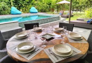 a wooden table with plates and wine glasses next to a pool at Villa Jeruk in Selong Belanak +14 photos