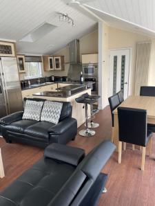a living room with black leather furniture and a kitchen at Labernum Lodge - Springhouse Country Park in Slaley