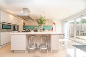 メイデンヘッドにある6 bedrooms beautiful home 3 bathrooms, quiet location with garden near Legoland Windsor Heathrowの白いキャビネットとスツール付きの大きな島のあるキッチンが備わります。