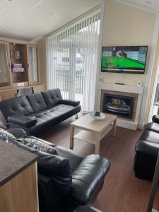 a living room with black leather furniture and a flat screen tv at Labernum Lodge - Springhouse Country Park in Slaley