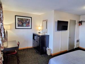 Cette chambre comprend un lit, un bureau et une télévision. dans l'établissement Woodland Inn, à Niagara Falls