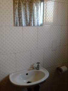 ein weißes Bad mit einem Waschbecken und einem Fenster in der Unterkunft Sunshinevibe guest house in Kasane