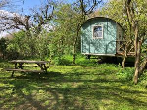 un tavolo da picnic e una roulotte verde in un campo di The Woodpecker shepherd hut a Elmswell