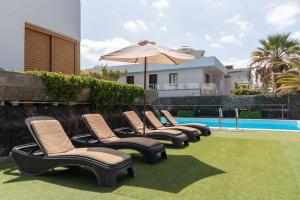 a row of chairs and an umbrella next to a pool at Villa Las Americas in Playa de las Americas