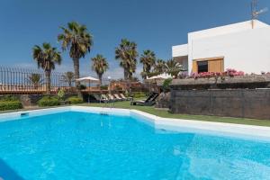 a swimming pool in front of a house with palm trees at Villa Las Americas in Playa de las Americas