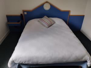 a white bed with a blue headboard and a pillow at initial by balladins Sable sur Sarthe in Sablé-sur-Sarthe