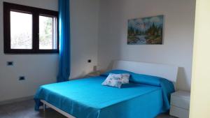 Cama azul en habitación blanca con ventana en Casa Marcella, en Dorgali