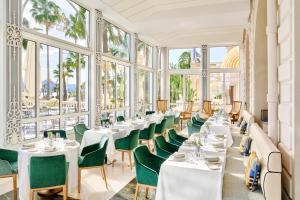 um restaurante com mesas brancas, cadeiras verdes e janelas em Carlton Cannes, a Regent Hotel em Cannes