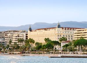 - un grand bâtiment à côté d'une étendue d'eau dans l'établissement Carlton Cannes, a Regent Hotel, à Cannes