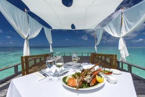 une table avec une assiette de nourriture et l'océan dans l'établissement Baros Maldives, à Malé