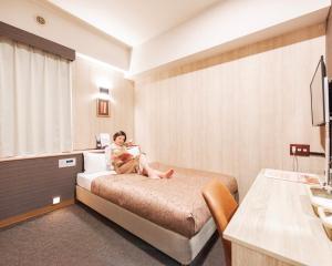 a woman sitting on a bed in a hotel room at HOTEL RELIEF Kokura Station in Kitakyushu