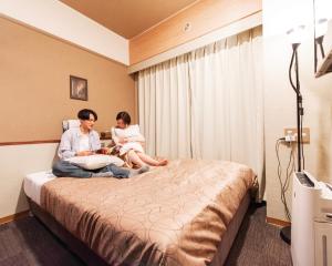 un homme et une femme assis sur un lit dans une chambre d'hôtel dans l'établissement HOTEL RELIEF Kokura Station, à Kitakyūshū