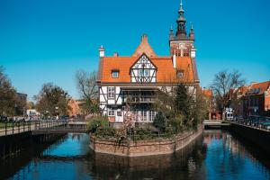 a building with a clock tower next to a river at The Old Fisherman's Nest by TriApart in Gdańsk