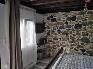 sypialnia z kamienną ścianą z łóżkiem i oknem w obiekcie Ελαιώνας - Solar Energy House w mieście Chorefto