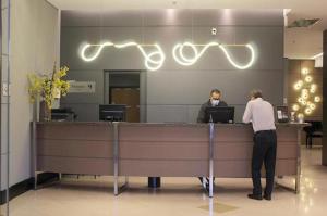 two people standing at a reception counter in an office at Araucária Flat Apto 305 in Ribeirão Preto