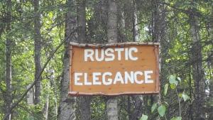 a sign that reads rustic elegance attached to a tree at Rustic Elegance in Talkeetna