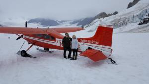 um homem e uma mulher ao lado de um avião vermelho na neve em Rustic Elegance em Talkeetna