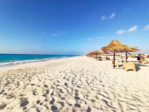 - une plage de sable avec des parasols en paille et l'océan dans l'établissement شاليه جديد عائلي كبير, à Dawwār al Ḩajj Aḩmad