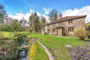 a stone house with a stream in front of it at Ford Cottage in Corscombe