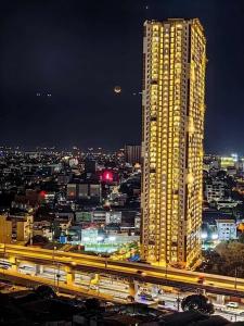 a tall yellow building in a city at night at 1 BR Condo Unit at The Celandine Condominium near Ayala Cloverleaf Mall in Manila
