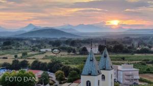 una iglesia con la puesta de sol en las montañas al fondo en Tiny guest house in peaceful part of Međugorje, en Međugorje