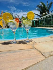 two wine glasses with fruit in them next to a swimming pool at Casa a 10 passos do mar - Temporada na Praia in Tamoios