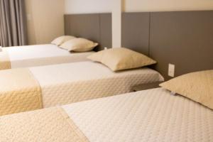 three beds in a room with white sheets and pillows at ESCARPAS FLATS in Capitólio