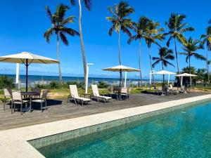 una piscina con mesas, sillas y sombrillas en Kalug - Duplex PÉ NA AREIA com 4 suítes, piscina e churrasqueira privativa na Praia do Sul! Perfeito para família - Wifi 300mb!, en Ilhéus