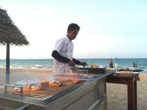 Un uomo che cucina cibo su una griglia sulla spiaggia di NN Beach Resort Nilaveli a Nilaveli