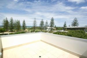 a balcony with a white wall and trees at 1 20 Kingfisher Drive Peregian Beach in Peregian Beach