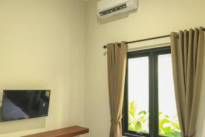 Zimmer mit einem TV und einem Fenster mit Vorhängen in der Unterkunft RedDoorz Syariah near Stasiun Madiun 2 in Madiun