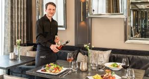 Un hombre está sirviendo vino en un restaurante en Victor's Residenz-Hotel Gummersbach, en Gummersbach