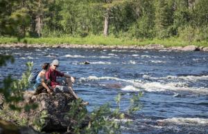un hombre y una mujer sentados en una roca en un río en Wilderness Hotel Juutua, en Inari