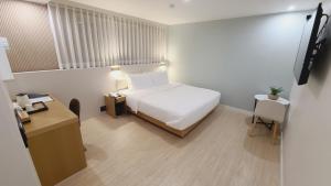 um quarto com uma cama branca, uma secretária e uma mesa em Hotel Andrest em Busan