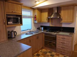 a kitchen with wooden cabinets and a stove top oven at 6 BERTH DELUXE CARAVAN PG73 GOLDEN PALM in Chapel Saint Leonards