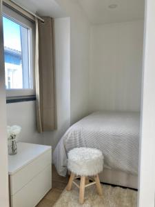 Dormitorio blanco con cama y taburete en Alojamento confortável a 2 min da Praia en Horta