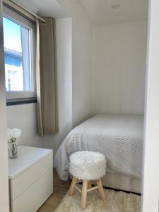 une chambre blanche avec un lit et un tabouret dans l'établissement Alojamento confortável a 2 min da Praia, à Horta