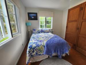 a bedroom with a bed with a blue comforter and windows at La Petite Ferme Manor Kerikeri in Kerikeri