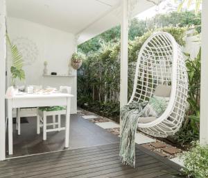 a white wicker chair sitting on a porch with a table at The White Cottage Byron Bay in Suffolk Park